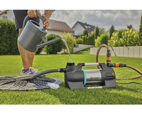 Osoba plní zahradní čerpadlo konví na zalévání na zahradě