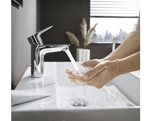 Fotografie koupelny s umyvadlem, kde si osoba myje ruce pod kohoutkem.