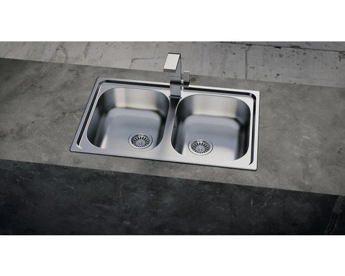 Nerezový dvoudřez s vodovodní baterií na betonovém povrchu