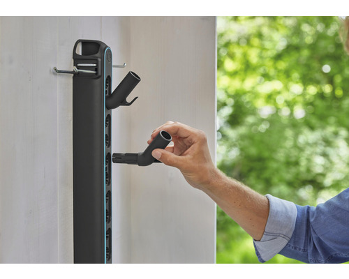 Držák zahradního nářadí na stěnu s osobou připevňující hadicovou přípojku