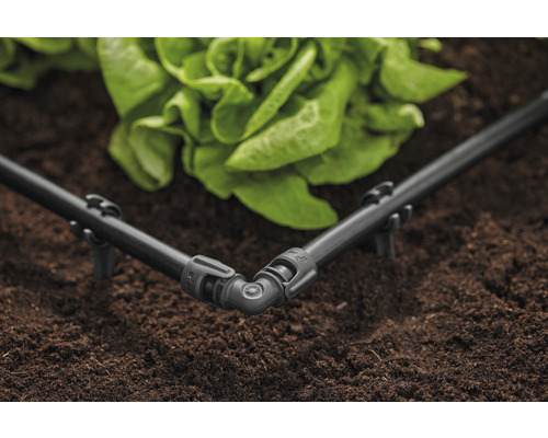 Rohový díl zavlažovacího systému s kapkovací hadicí v zahradním záhonu