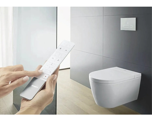 Osoba ovládá sprchové WC pomocí dálkového ovladače a nástěnného ovládacího panelu v koupelně.