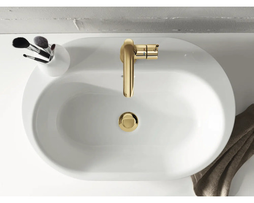 Pohled shora na bílé umyvadlo se zlatou baterií a nádobou se štětci na make-up