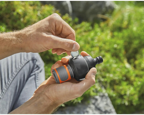 Osoba vkládá minci do zahradního časovače vody.