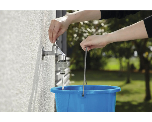Osoba plní modrý kbelík vodou z venkovního kohoutku.