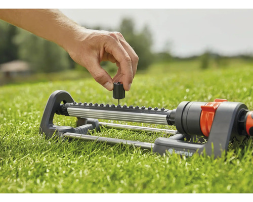 Osoba nastavuje obdélníkový zavlažovač Gardena na trávníku.