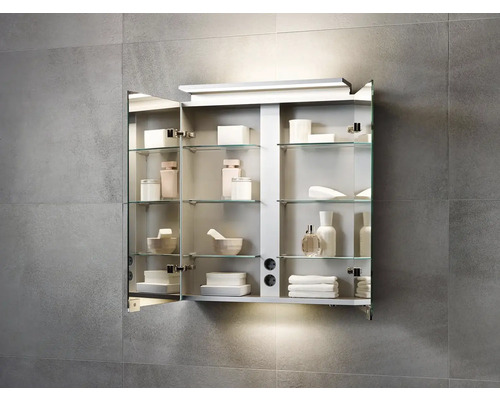 Otevřená zrcadlová skříňka se skleněnými policemi a různými koupelnovými potřebami na šedé stěně