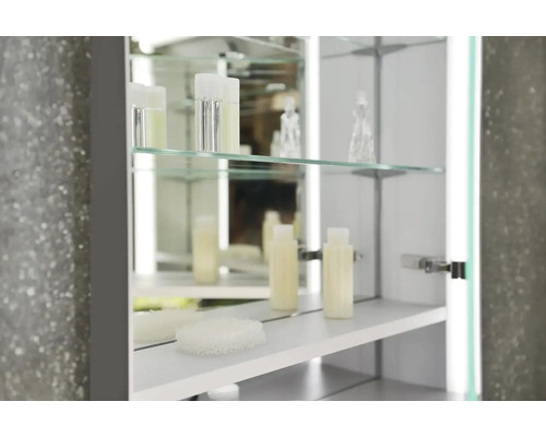 Otevřená zrcadlová skříňka se skleněnými policemi a pečujícími produkty