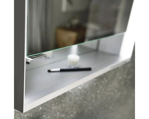 Detailní pohled na zrcadlovou skříňku s policí, na které je svíčka a štětec