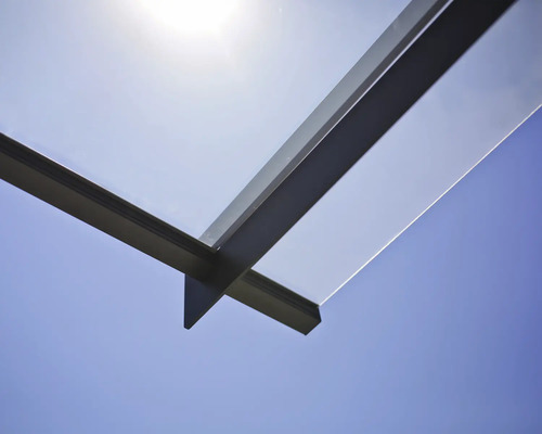 Detail terasového zastřešení ze skla a kovu na pozadí modré oblohy