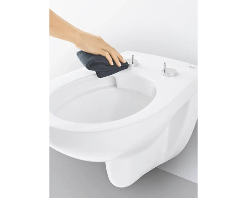 Ruka čistí bílou závěsnou toaletu hadříkem.