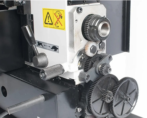 Detailní záběr soustruhu s ozubenými koly a pákami.