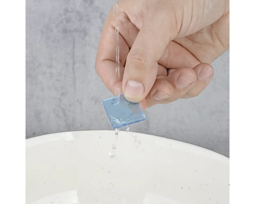 Ruka drží modrý čtvercový kus materiálu pod proudem vody.