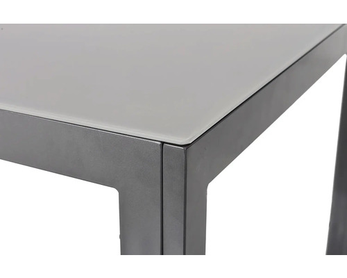 Detail stolu se skleněnou deskou a kovovým rámem.