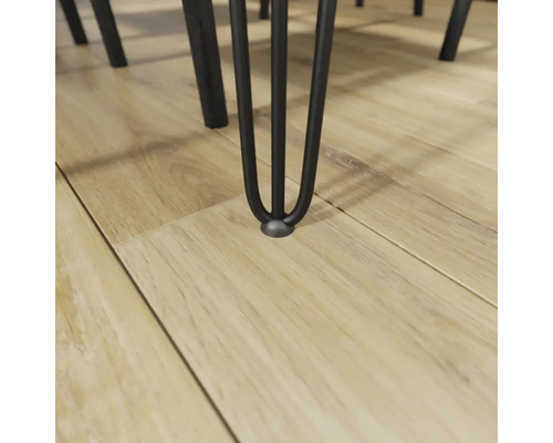 Detailní záběr kovové nohy stolu na dřevěné podlaze.