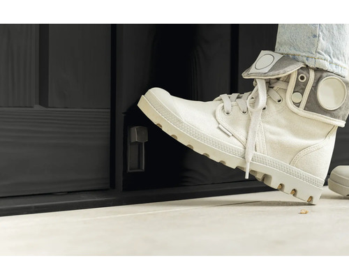 Osoba otevírá nohou černé venkovní dveře s otočným knoflíkem