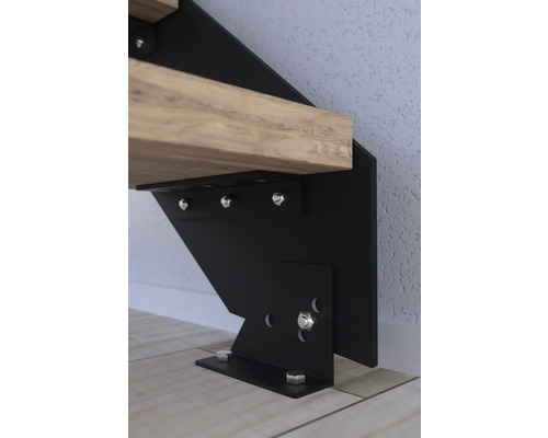 Detailní záběr upevnění schodiště z černého kovu s dřevěným stupněm, upevněného šrouby.