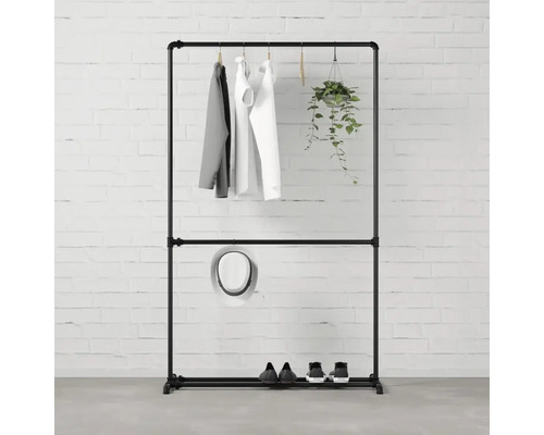 Černý stojan na šaty s oblečením, kloboukem, botami a závěsnou rostlinou před cihlovou zdí.