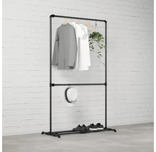 Černý věšák na šaty s oblečením, kloboukem, botami a rostlinou před cihlovou zdí