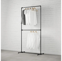 Černý věšák na oblečení se dvěma úrovněmi a oblečením na dřevěných ramínkách před cihlovou zdí