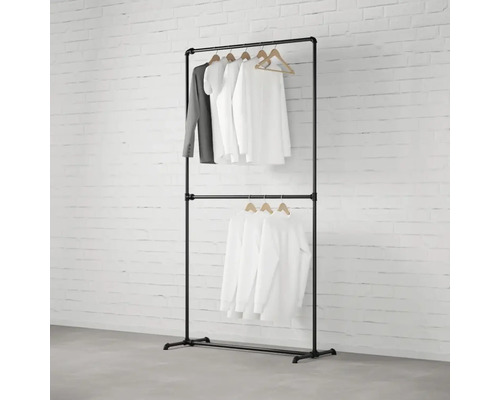 Černý věšák na oblečení se dvěma úrovněmi a oblečením na dřevěných ramínkách před cihlovou zdí