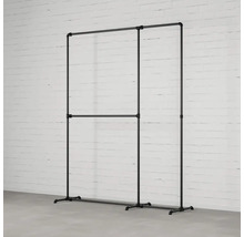 Věšák na šaty z trubek před cihlovou zdí