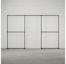 Černá, modulární šatní skříň se stojanem na oděvy z kovových trubek na pozadí bílé cihlové zdi.