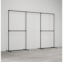 Šatní stojan z ocelových trubek v industriálním designu před bílou cihlovou zdí.