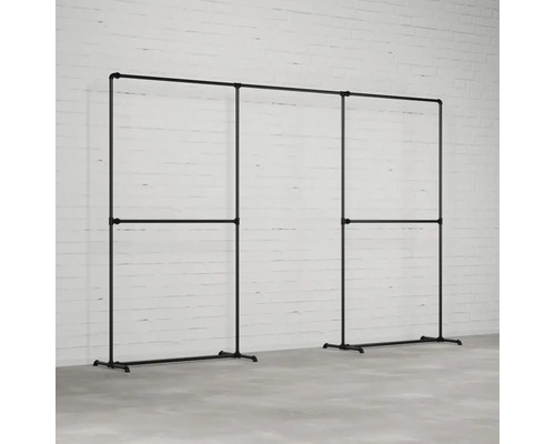 Šatní stojan z ocelových trubek v industriálním designu před bílou cihlovou zdí.