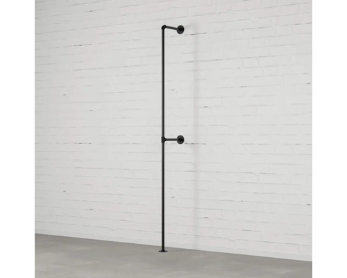 Černý kovový věšák na šaty z trubek u bílé cihlové zdi