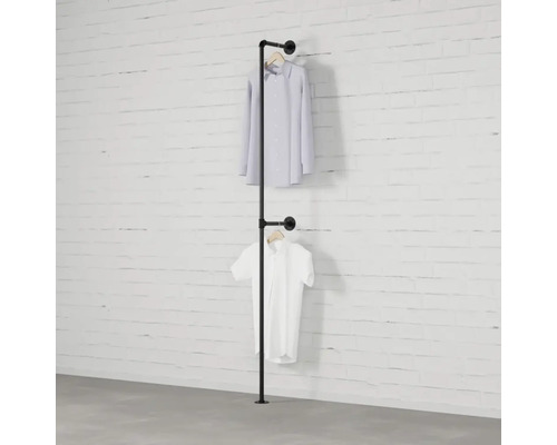 Železný trubkový věšák na šaty se dvěma košilemi visícími před bílou cihlovou zdí