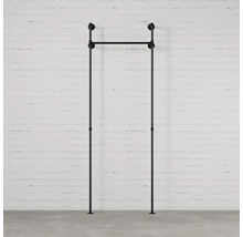 Černý věšák na oblečení z kovových trubek před bílou cihlovou zdí