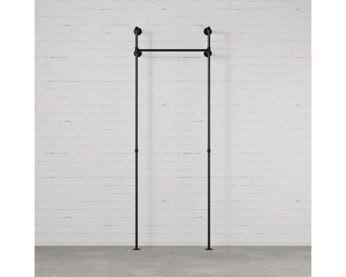 Černý věšák na oblečení z kovových trubek před bílou cihlovou zdí