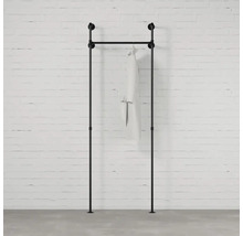 Černá šatní tyč z trubek s oděvem před cihlovou zdí