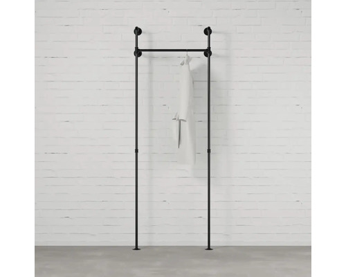 Černá šatní tyč z trubek s oděvem před cihlovou zdí