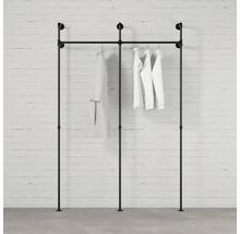 Černý stojan na šaty z trubek s oblečením u zdi