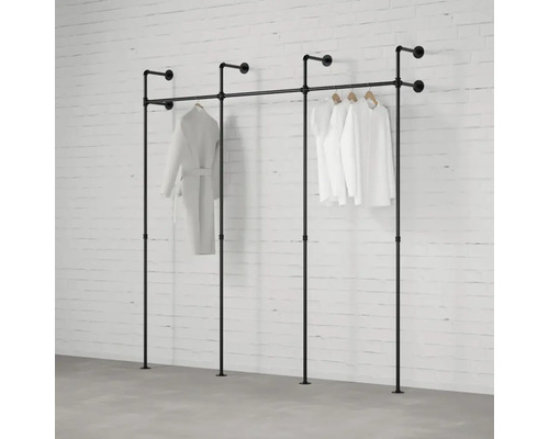 Černý trubkový systém na šaty se zavěšeným oblečením před cihlovou zdí