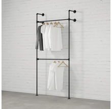 Dvouřadý věšák na šaty z kovových trubek se zavěšeným oblečením před cihlovou zdí