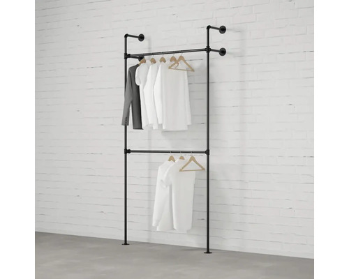 Dvouřadý věšák na šaty z kovových trubek se zavěšeným oblečením před cihlovou zdí