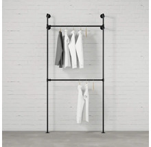 Stojan na oblečení z trubek se zavěšeným oblečením před cihlovou zdí