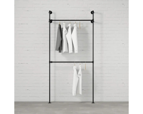 Stojan na oblečení z trubek se zavěšeným oblečením před cihlovou zdí