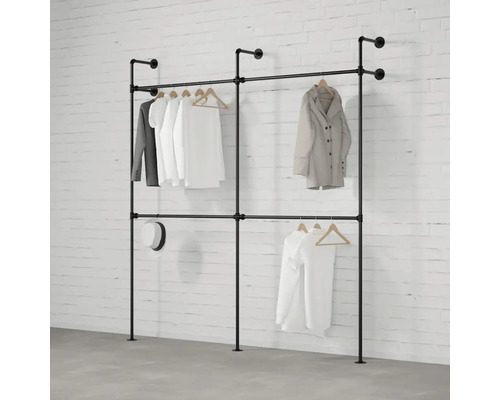 Věšák na šaty z trubek se zavěšeným oblečením před cihlovou zdí