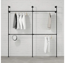 Volně stojící šatní tyč z trubek se zavěšeným oblečením na pozadí bílé cihlové zdi.