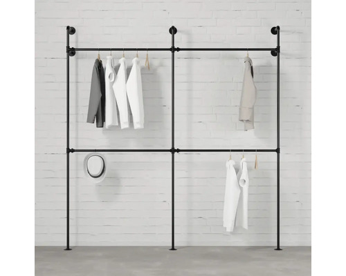 Volně stojící šatní tyč z trubek se zavěšeným oblečením na pozadí bílé cihlové zdi.