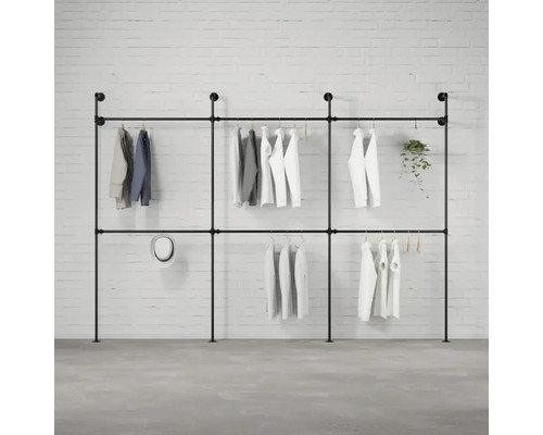 Černý kovový trubkový věšák na šaty s oblečením před cihlovou zdí