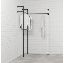 Černý věšák na oblečení z kovových trubek s oblečením před cihlovou zdí