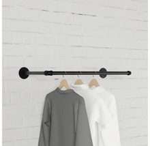 Nástěnná šatní tyč z kovové trubky s oblečením na dřevěných ramínkách před cihlovou zdí