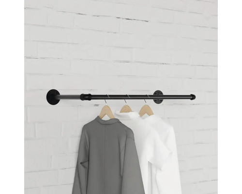 Nástěnná šatní tyč z kovové trubky s oblečením na dřevěných ramínkách před cihlovou zdí