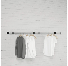 Černá šatní tyč se zavěšeným oblečením před cihlovou zdí