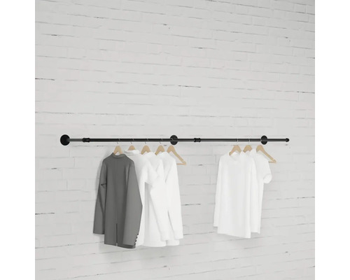 Černá šatní tyč se zavěšeným oblečením před cihlovou zdí